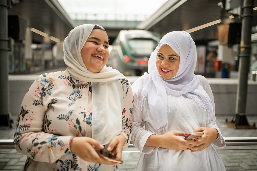 Two young woman at the train station using mobile phone