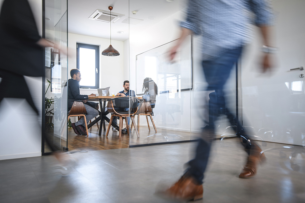 Blurred motion of male and female businesspeople walking down hallway contrasted by still and careful debate of new ideas in the conference room.