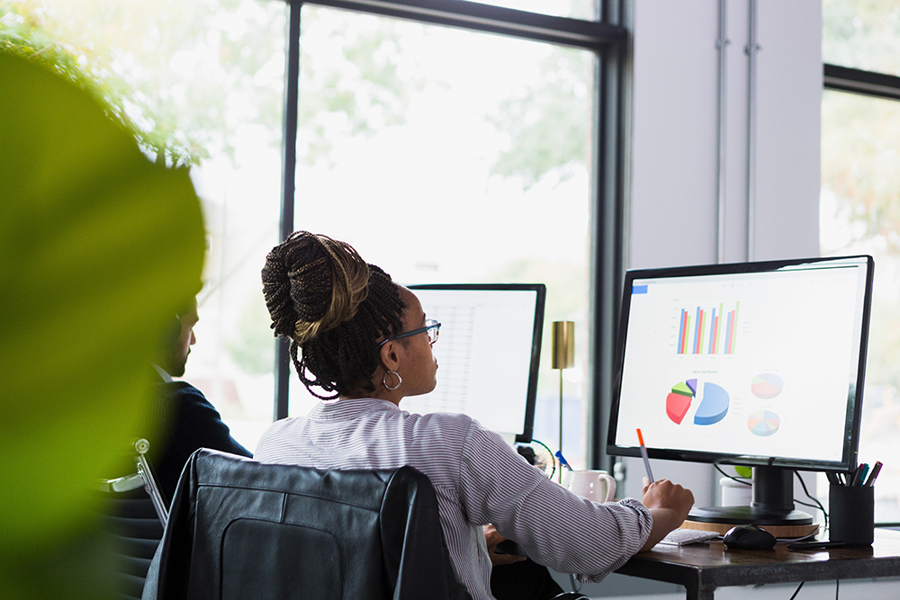 A rear view photo of a mid adult woman working on graphs for a presentation.