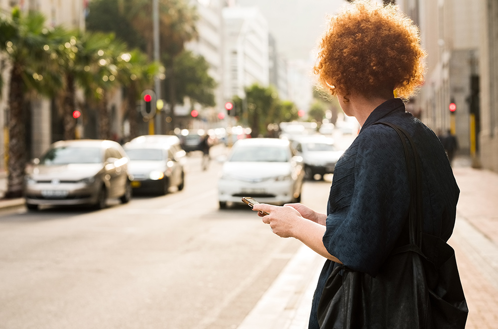 Shot of a mature woman standing by the city street with a mobile phone waiting for the taxi