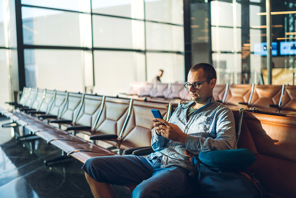 Young handsome caucasian man Killing Time Before a Flight. Using his smart phone.