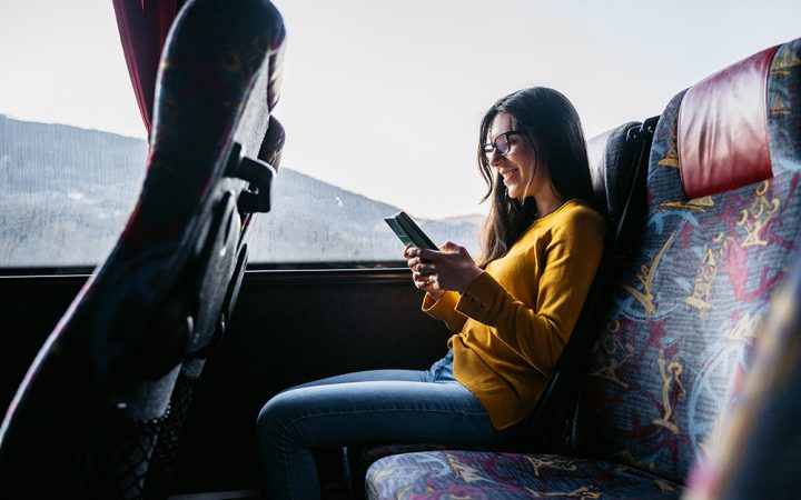 Young beautiful Caucasian woman reading news or checking social media on smartphone while traveling by bus.