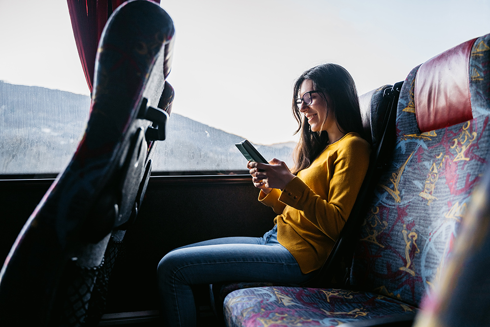 Young beautiful Caucasian woman reading news or checking social media on smartphone while traveling by bus.