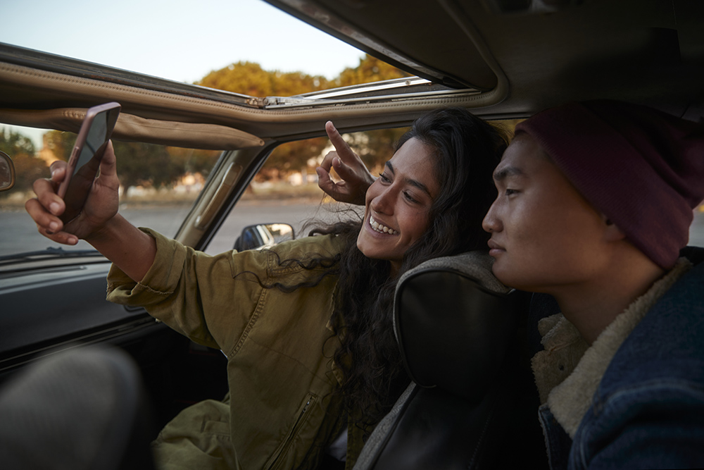Young mixed race hipster couple taking selfie with mobile phone inside car