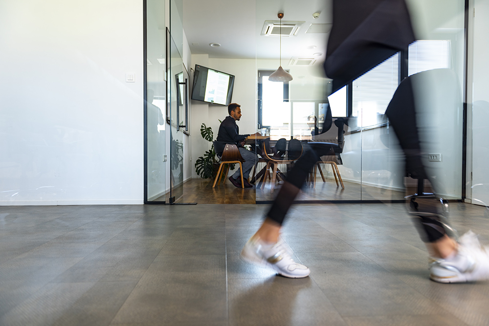 Blurred motion of male and female businesspeople walking down hallway contrasted by still and careful debate of new ideas in the conference room.