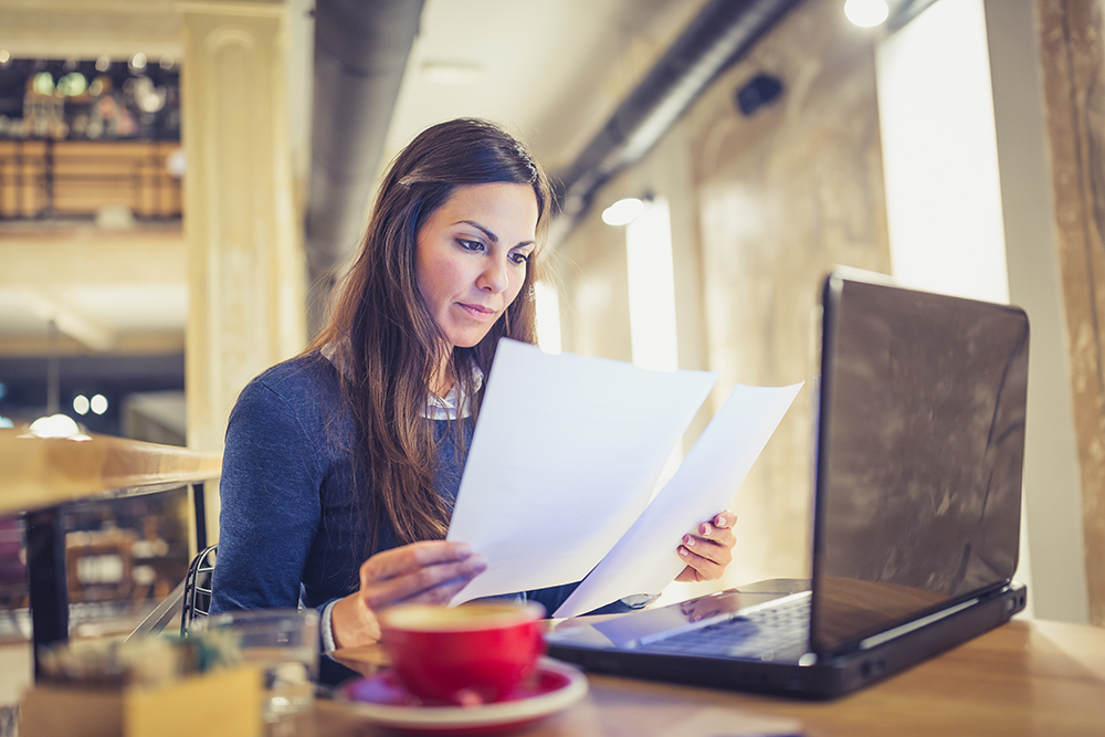 Pretty black hair young woman sitting in cafe, drinking coffee, browsing documents,using laptop