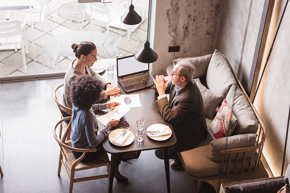 Two female colleagues having business meeting in high end restaurant with senior client. Multi-ethnic group. High angle view