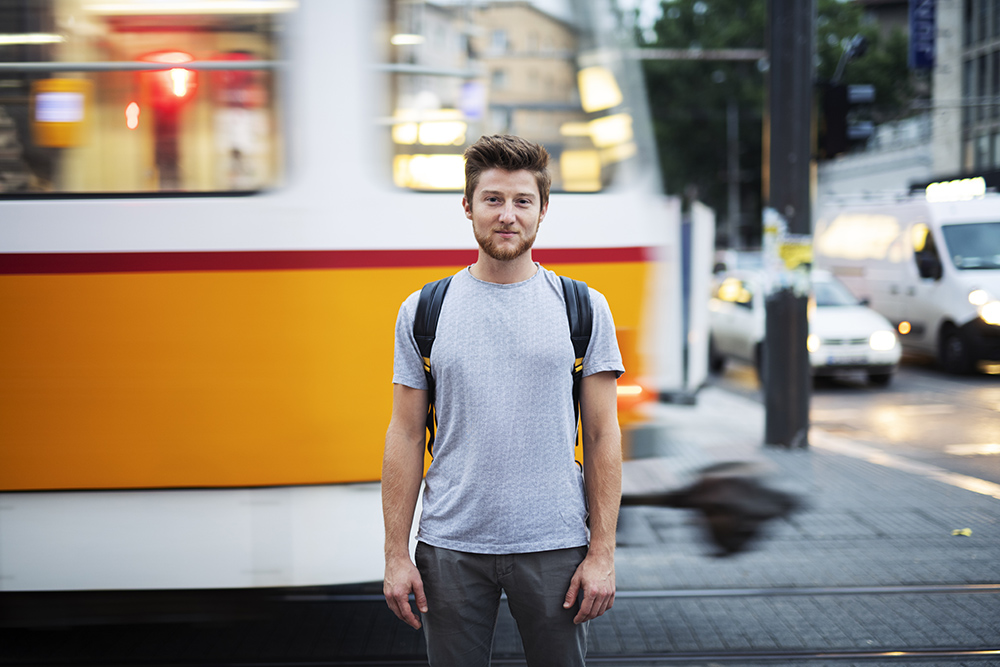 Male portrait on the city street around tramway, he standing in front of blurred motion tramway and vehicles on background and looking at camera.