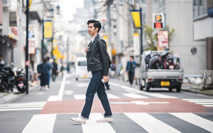 Young Japanese man striding through pedestrian zebra crossing on a relaxing city break in urban Tokyo.