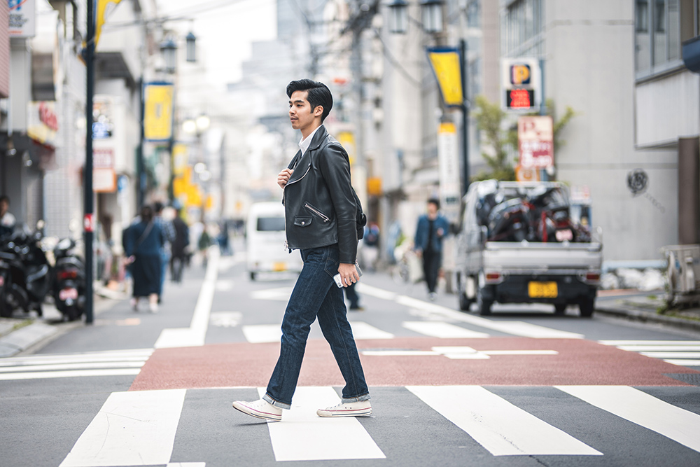 Young Japanese man striding through pedestrian zebra crossing on a relaxing city break in urban Tokyo.