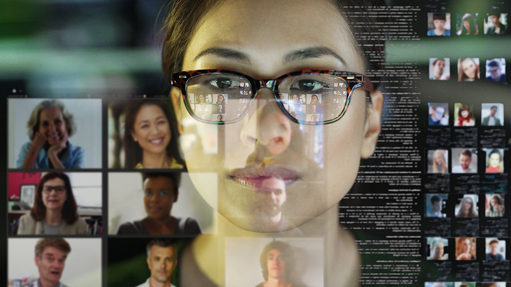 Stock photograph of a professional Asian woman, in her office, looking at a see through display with a team of people making a conference call.