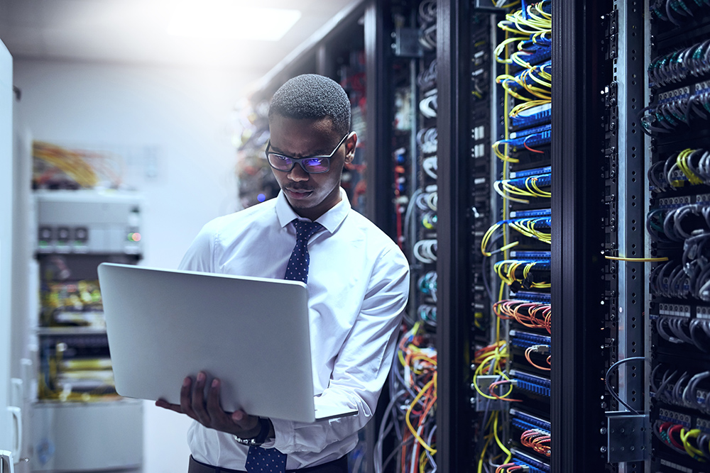 Cropped shot of a IT technician working on his laptop while standing inside of a server room