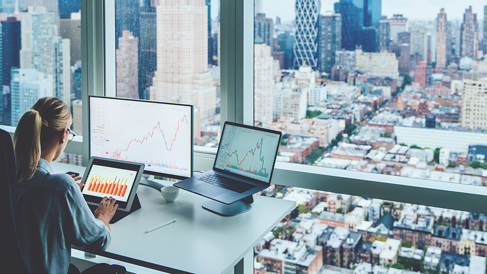Back view of business woman sitting at panoramic skyscraper office desktop front PC computer with financial graphs and statistics on monitor.Analysis of digital market and investment in block chain Back view of business woman sitting at panoramic skyscraper office desktop front PC computer with financial graphs and statistics on monitor.Analysis of digital market and investment in block chain