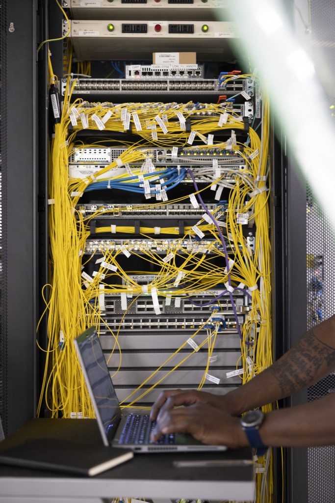 A man works on his laptop aside a server in a data centre