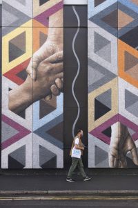 Hipster-looking man with a Colt bag walking past a Connectivity mural