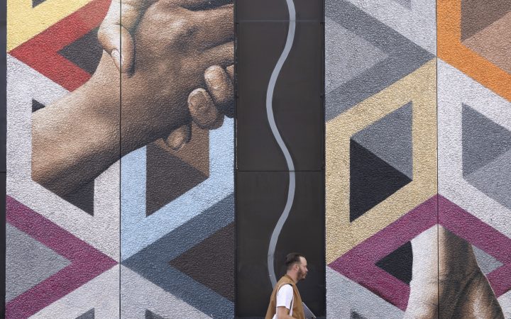 Hipster-looking man with a Colt bag walking past a Connectivity mural