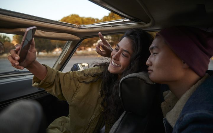 Two people look at a smart phone, sat in a car