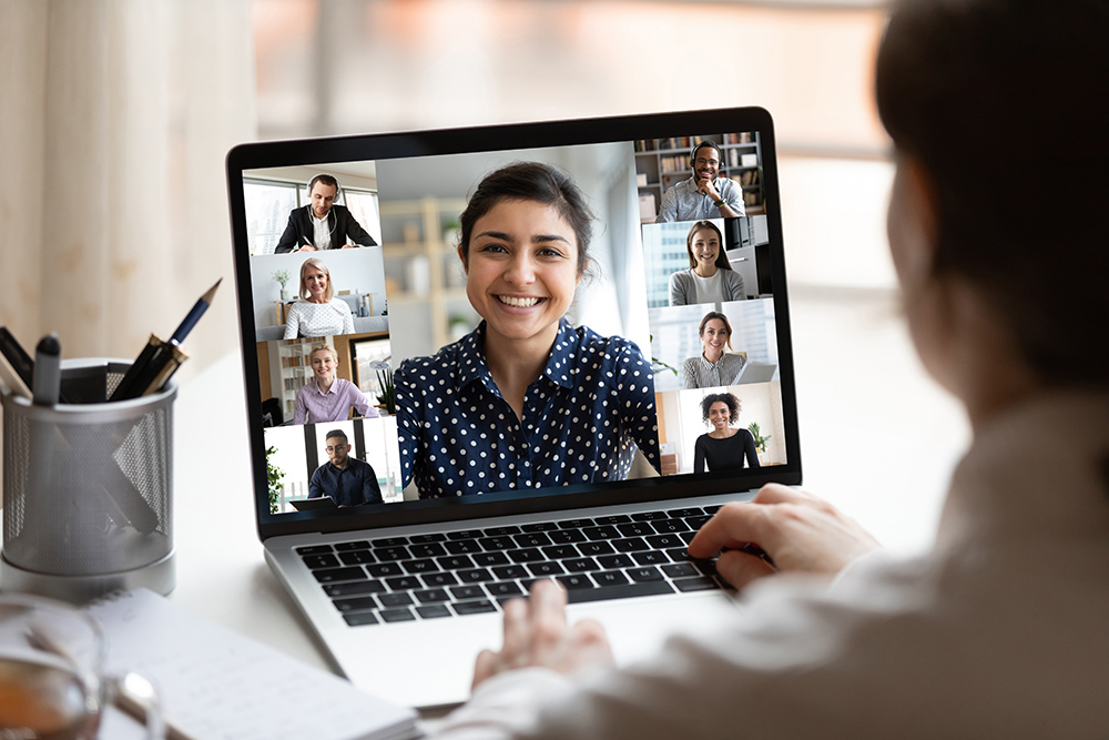 Indian lady lead videocall, pc screen view over woman shoulder Woman sit at desk looking at computer screen where collage of diverse people webcam view. Indian ethnicity young woman lead video call distant chat, group of different mates using videoconference app