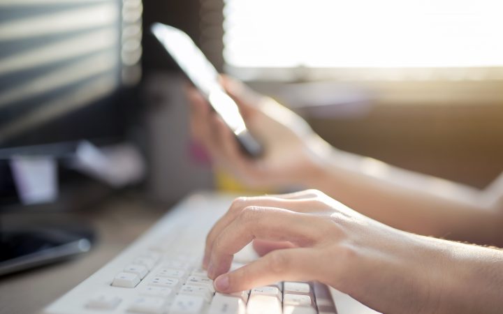 Close up of hand using a mobile phone and typing on a keyboard