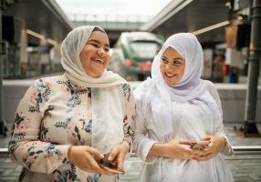 Two young woman at the train station using mobile phone