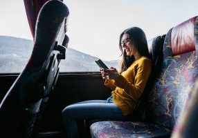 Young beautiful Caucasian woman reading news or checking social media on smartphone while traveling by bus.