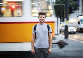 Male portrait on the city street around tramway, he standing in front of blurred motion tramway and vehicles on background and looking at camera.