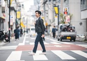 Young Japanese man striding through pedestrian zebra crossing on a relaxing city break in urban Tokyo.