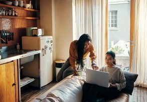Shot of two attractive young women drinking coffee and using a laptop while relaxing together at home over the weekend