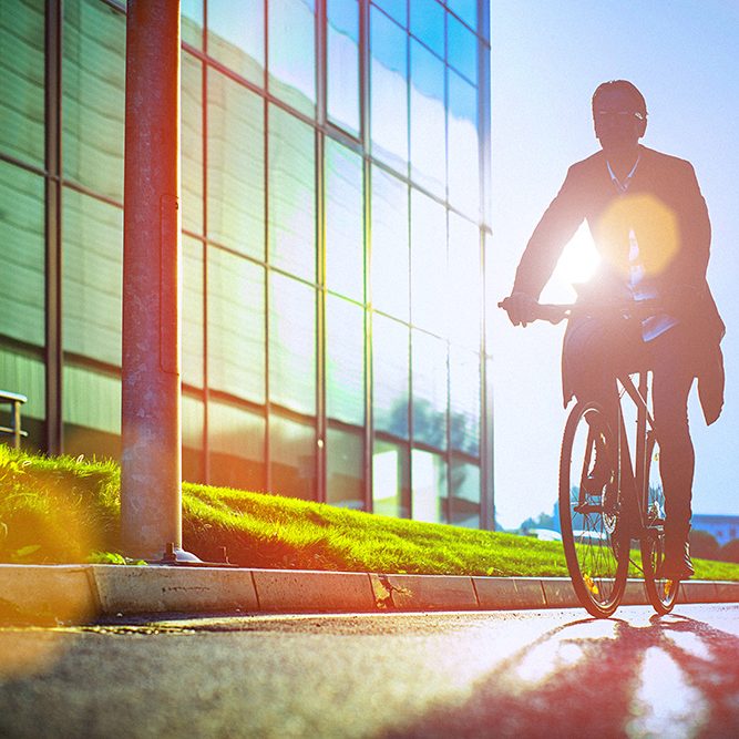 Handsome man, on the way to work, riding bicycle beside the modern office building. The man is casually dressed and wears eyeglasses and carries black briefcase hung on shoulder. Blurred motion, copy space has been left.