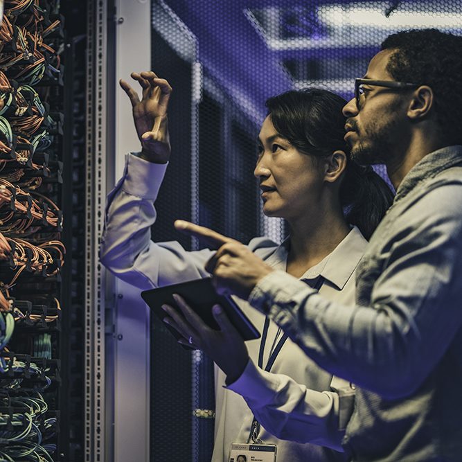Female Asian IT technician explaining network connection to a novice engineer Side view of a female Asian IT engineer explaining network connections in a server to a novice African-American technician.