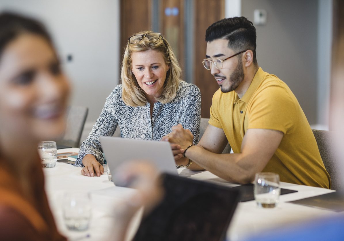 Hipster young man showing female colleague laptop Mature businesswoman smiling with employee, working together, collaboration, teamwork